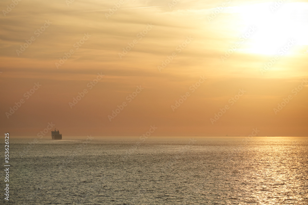 Commercial cargo ship sailing across vast North Sea with golden sunset sky