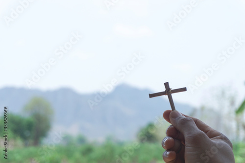 The hands of an Asian man hold a cross, a symbol of Christianity, to ask for blessings or protect from evil or invisible things with green mountain far and blurred with free space on the left side.
