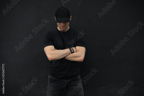 Man in cap with crossed arms standing against black wall
