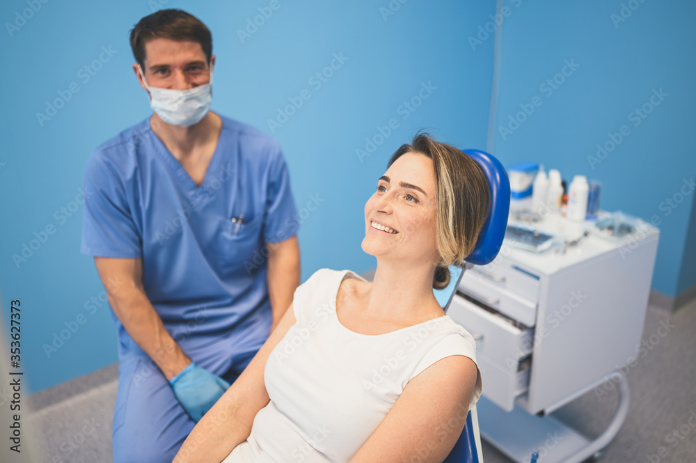 Dentist examining a patient's teeth using dental equipment in dentistry office. Stomatology and health care concept. Young handsome male doctor in disposable medical facial mask, smiling happy woman.
