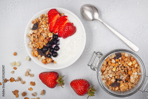 Bowl of homemade granola with yogurt and fresh berries on white background from top view