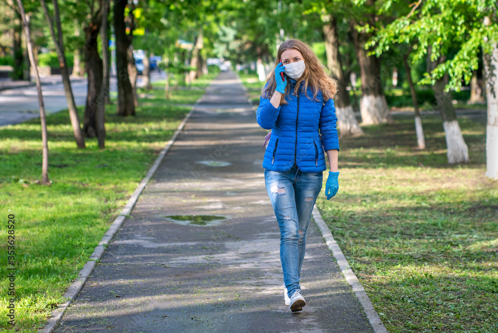 A woman in protective mask and gloves is walking along empty street and talking on phone. Lifestyle and safe behavior during a coronavirus pandemic. The new normal and modern reality. Copy space. A woman in protective mask and gloves is walking along empty street and talking on phone. Lifestyle and safe behavior during a coronavirus pandemic. The new normal and modern reality. Copy space.