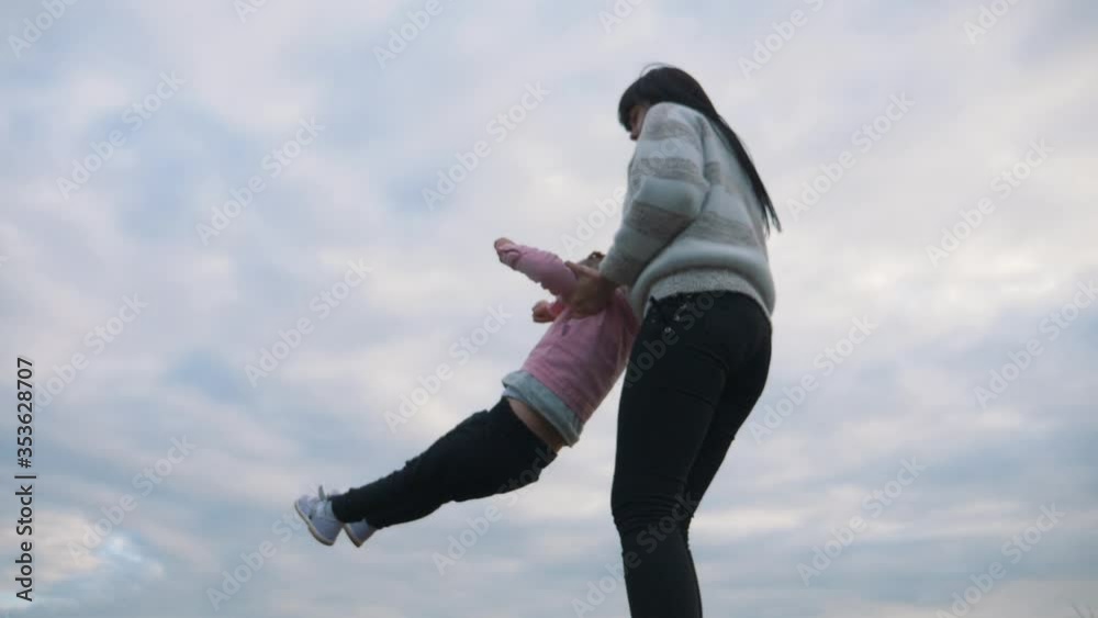 A young mother holds her happy little child in her arms and circles it in the open air in the countryside. A happy family spends their weekends enjoying a good holiday. A young mother holds her happy little child in her arms and circles it in the open air in the countryside. A happy family spends their weekends enjoying a good holiday.
