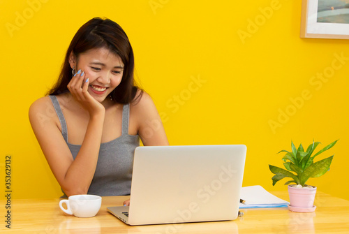 asian woman smiling and looking at a laptop computer on a wooden table