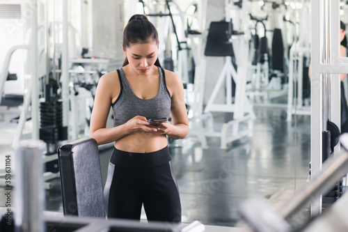 Beautiful Asian women, Thai people wearing exercise clothes, standing, watching and typing mobile phone messages in the gym. In the exercise concept Is any physical activity that enhances or maintains