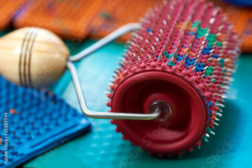 A red hand massager with rubber and spikes, metal needles, lies on a green mat. Promotional, thematic and subject photography. For relaxation and health