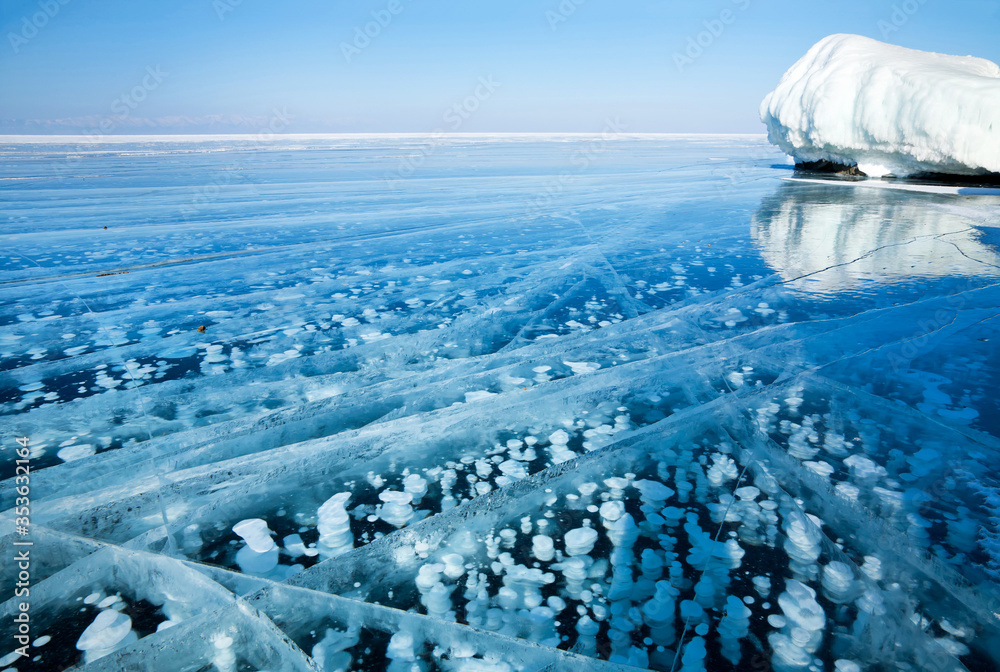 Magnificent winter landscape with clear transparent ice of Siberian Baikal Lake. White bubbles of bottom gases frozen into the ice near the icy cliffs of Olkhon Islands. Natural unusual background