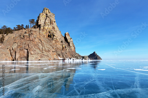 Beautiful winter landscape of Lake Baikal with clear blue ice near the rocks of Peschanaya Bay. A group of tourists travels near the famous cliff Small Belfry photo