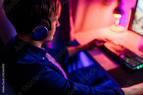 gamer playing computer games online with headphones  in a room with neon light.