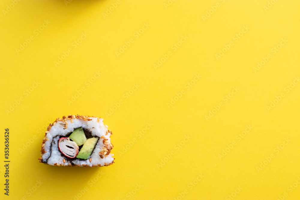 Homemade single piece of homemade sushi roll. Isolated on yellow background. Avocado, surimi and cucumber with fried sesame seeds, california roll Homemade single piece of homemade sushi roll. Isolated on yellow background. Avocado, surimi and cucumber with fried sesame seeds, california roll