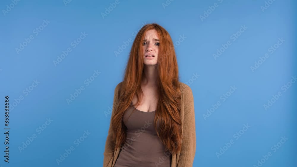 Redheaded woman in brown t-shirt and cardigan. She looking upset and showing blah blah blah sign, posing against blue studio background. Close up Redheaded woman in brown t-shirt and cardigan. She looking upset and showing blah blah blah sign, posing against blue studio background. Close up