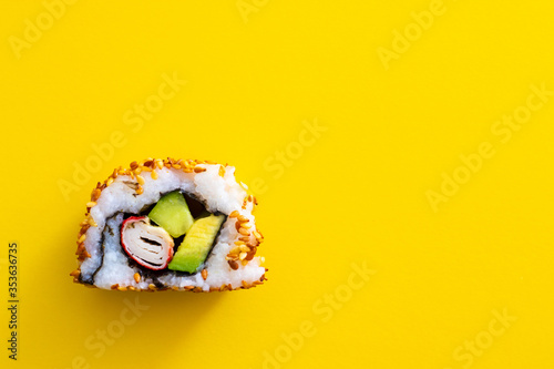 Homemade single piece of homemade sushi roll. Isolated on yellow background. Avocado, surimi and cucumber with fried sesame seeds, california roll photo