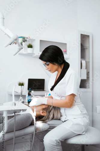 Stomatology doctor treating woman s teeth in dentistry clinic. Female dentist in white uniform and gloves using restoration instruments. Vertical photo