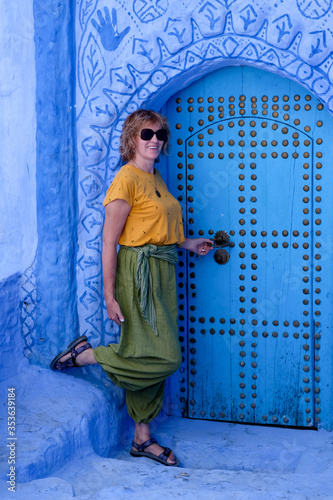 Pretty smiling woman standing near painted door in the blue city of Chefchaouen, Morocco.