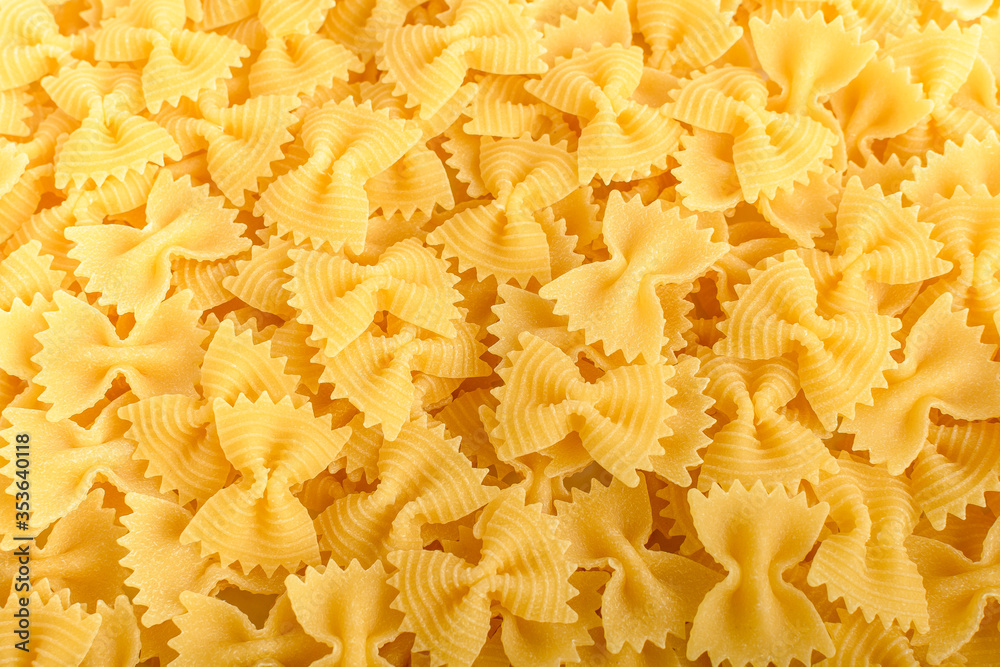 Heap of dried Farfalle Rigate Italian pasta ready to be cooked, isolated on a white table, top view or flat lay of healthy food 
