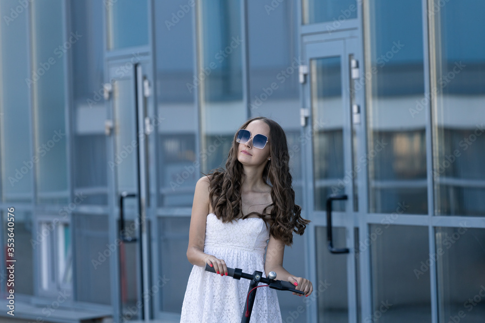 A beautiful brunette in a light dress rides an electric scooter around the city A beautiful brunette in a light dress rides an electric scooter around the city