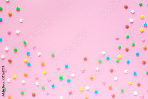 Colored sugar stars sprinkled as a half round frame on a pastel light pink backdrop. Background composition with copy space, top view