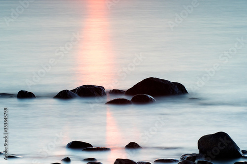 Sunset reflection into water surface next boulders, Sweden