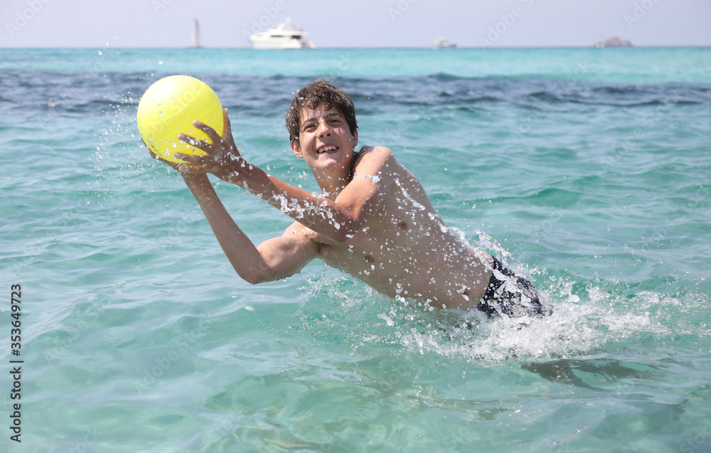 Young boy plays with a yellow ball on the sea