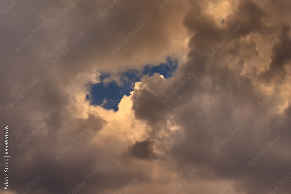 Piece of blue sky, surrounded by white clouds shaded by gray Piece of blue sky, surrounded by white clouds shaded by gray