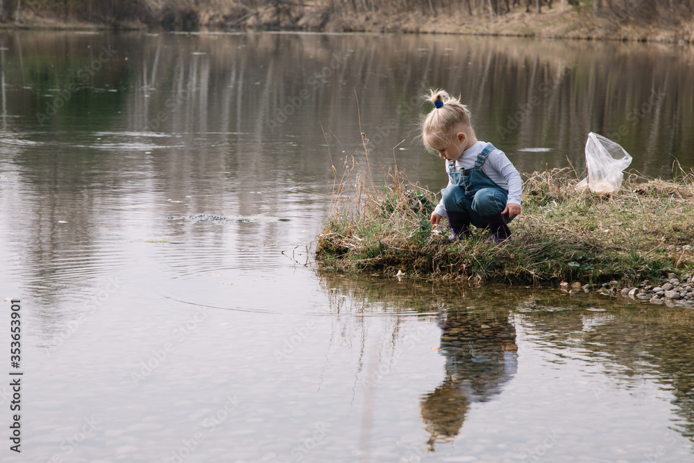Little girl in rubber boots catches and feeds fish on the river in a jar