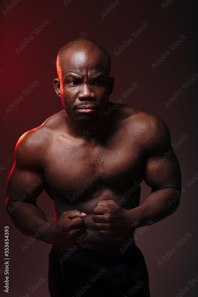 Vertical photo with red light. Muscular bodybuilder african american showing naked torso muscles and screaming. Vertical photo with red light. Muscular bodybuilder african american showing naked torso muscles and screaming.