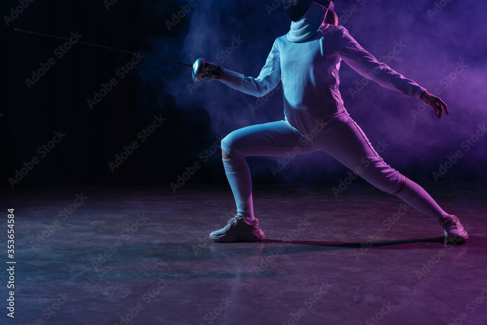 Cropped view of swordswoman fencing on black background with smoke and lighting