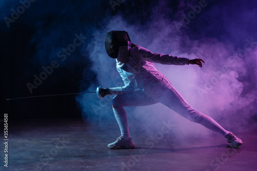 Swordswoman fencing with rapier on black background with colorful smoke