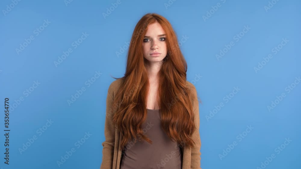Redheaded female in brown t-shirt and cardigan. She is showing stop sign by her palm and saying no while posing on blue background. Close up Redheaded female in brown t-shirt and cardigan. She is showing stop sign by her palm and saying no while posing on blue background. Close up