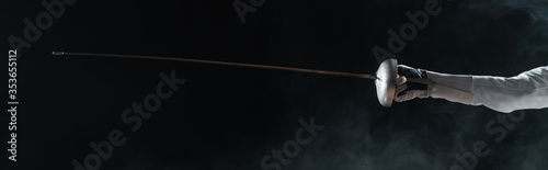 Canvas Print Panoramic orientation of fencer in glove holding rapier on black background with