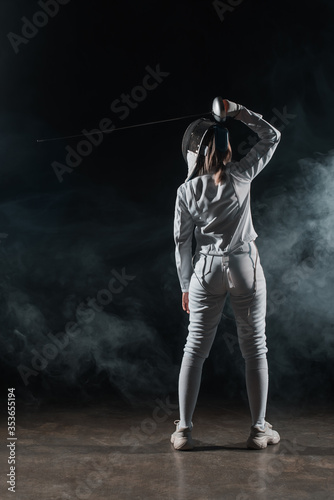 Back view of swordswoman fencing on black background with smoke
