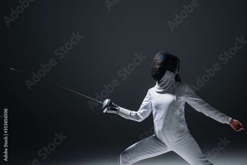 Fencer in fencing mask exercising on black background