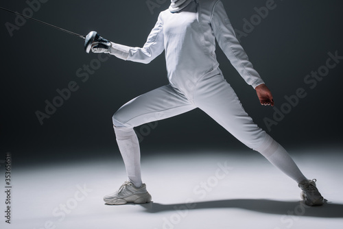 Cropped view of fencer in fencing suit training with rapier on white surface on black background