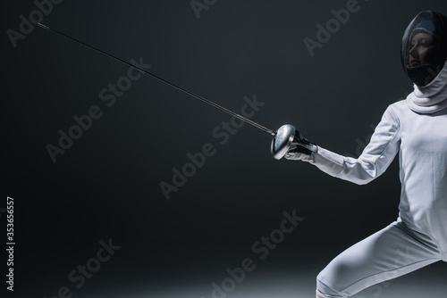 Cropped view of fencer in fencing mask holding rapier on black background