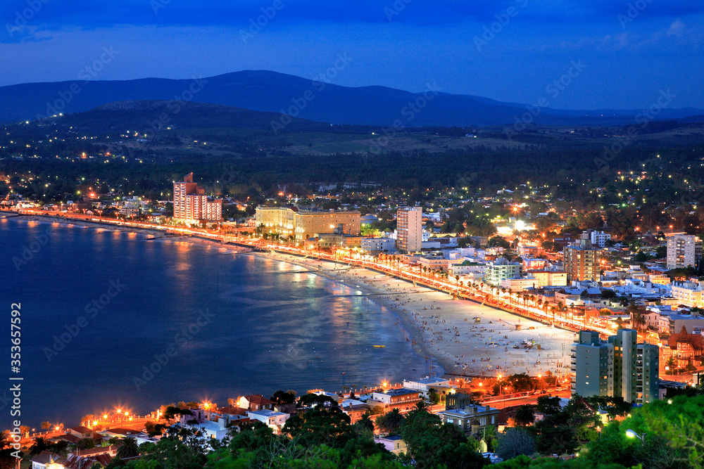 Aerial view of the beach and city, during twilight, with city lights and water reflections on the sea. Piriapolis, Uruguay.