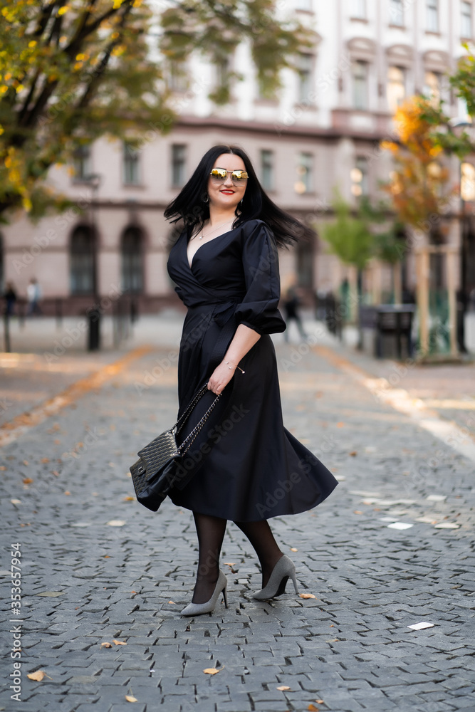 Autumn fashion outdoor. The girl with red lips in fashionable stylish black dress and sunglasses, autumnal lifestyle on the background of blurry yellow-green trees in the park. Vertical Autumn fashion outdoor. The girl with red lips in fashionable stylish black dress and sunglasses, autumnal lifestyle on the background of blurry yellow-green trees in the park. Vertical