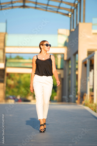 Front view of going woman on blur background of summer street. Female tourist walking along tropical resort hotel building
