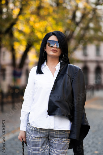 Autumn fashion outdoor. The girl in fashionable stylish white shirt , pants, jacket and sunglasses, autumnal lifestyle on the background of blurry yellow-green trees in the park. Vertical