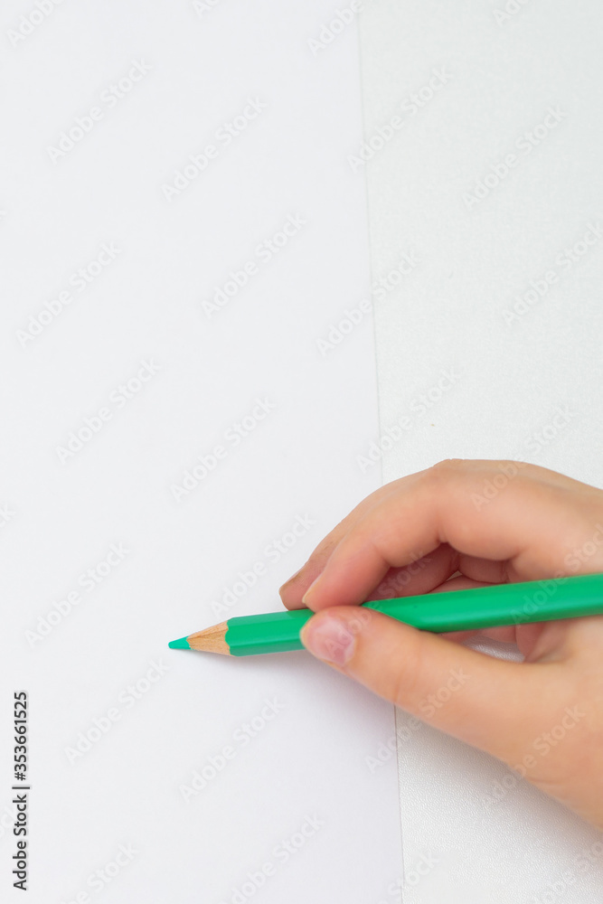 Top view of hand of child holding green color pencil on white paper with set of colour pencils. Copy space. Children's creativity. Top view of hand of child holding green color pencil on white paper with set of colour pencils. Copy space. Children's creativity.