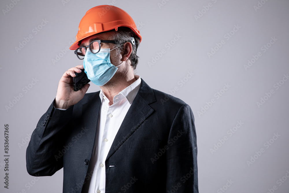 ingegnere con giacca casco arancione e mascherina chirurgica facciale fa una telefonata , isolato su sfondo bianco ingegnere con giacca casco arancione e mascherina chirurgica facciale fa una telefonata , isolato su sfondo bianco