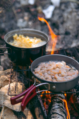 Cooking dinner in metal utensils for camping. Campfire at the campsite. Shrimp in white wine and pasta. Foldable portable dishes for tourists. Vertical photo. tourist bowler