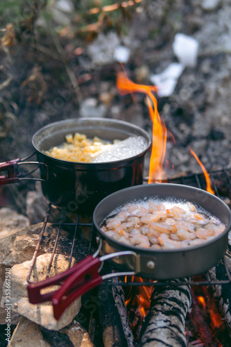 Cooking dinner in metal utensils for camping. Campfire at the campsite. Shrimp in white wine and pasta. Foldable portable dishes for tourists. Vertical photo