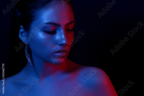 The young girl closeup in bright neon light. Fashionable high lighter makeup. The concept of the trend image and neon light.