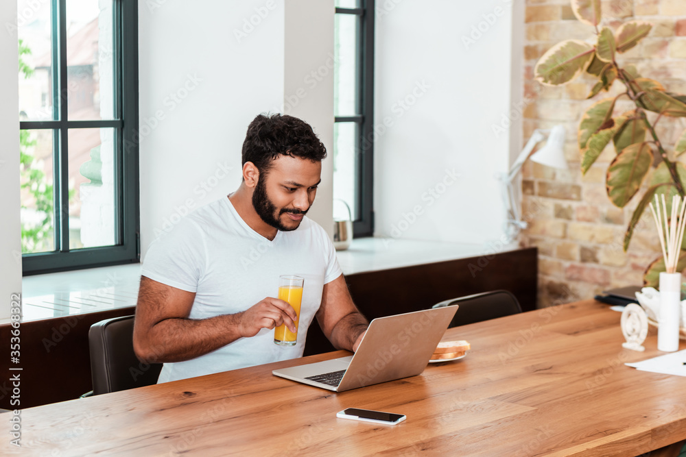 bearded african american freelancer working from home and holding glass of orange juice bearded african american freelancer working from home and holding glass of orange juice