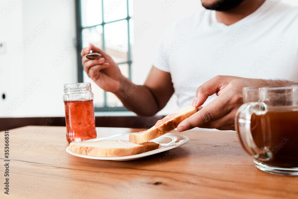 cropped view of african american man holding spoon near jar with sweet jam and toast bread on plate cropped view of african american man holding spoon near jar with sweet jam and toast bread on plate