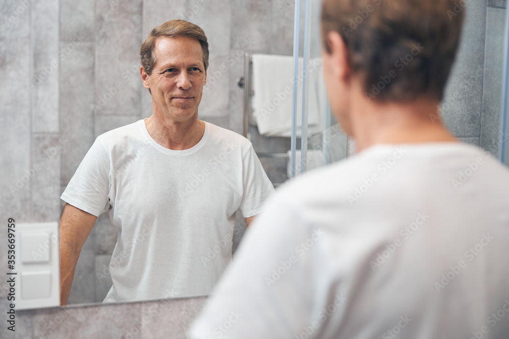 Obraz premium Contented middle-aged male looking at his appearance