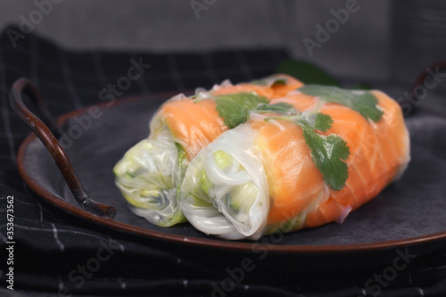 Two pieces of traditional Vietnamese spring rolls fied with salmon, avocado, salad and rice noodles on dark dish