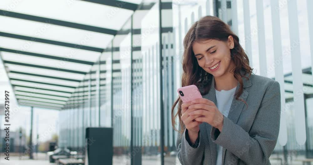 Young attractive businesswoman smiling and using smartphone near modern office building. Beautiful girl in smart casual clothes chatting in social networks while standing at street. Young attractive businesswoman smiling and using smartphone near modern office building. Beautiful girl in smart casual clothes chatting in social networks while standing at street.