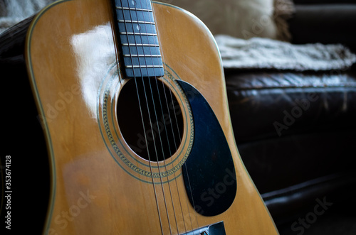 An acoustic guitar leaning on a rustic old leather sofa.