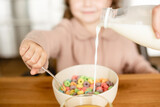 selective focus of milk pouring into bowl with tasty corn flakes near cute kid